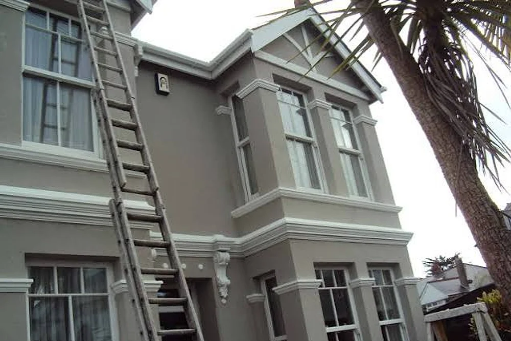 Ladders up to a rendered Victorian semi during exterior painting